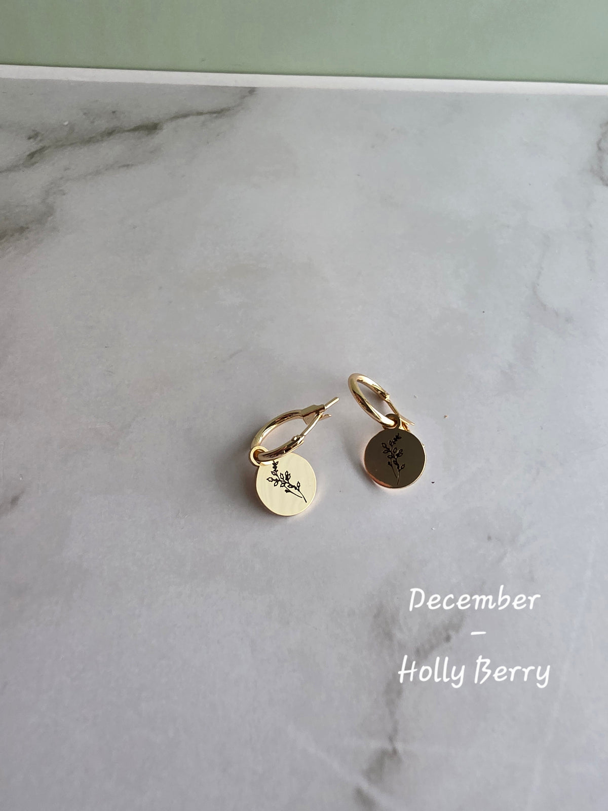 Dainty birth flower earrings with engraved charms on 18K gold-plated huggie hoops.