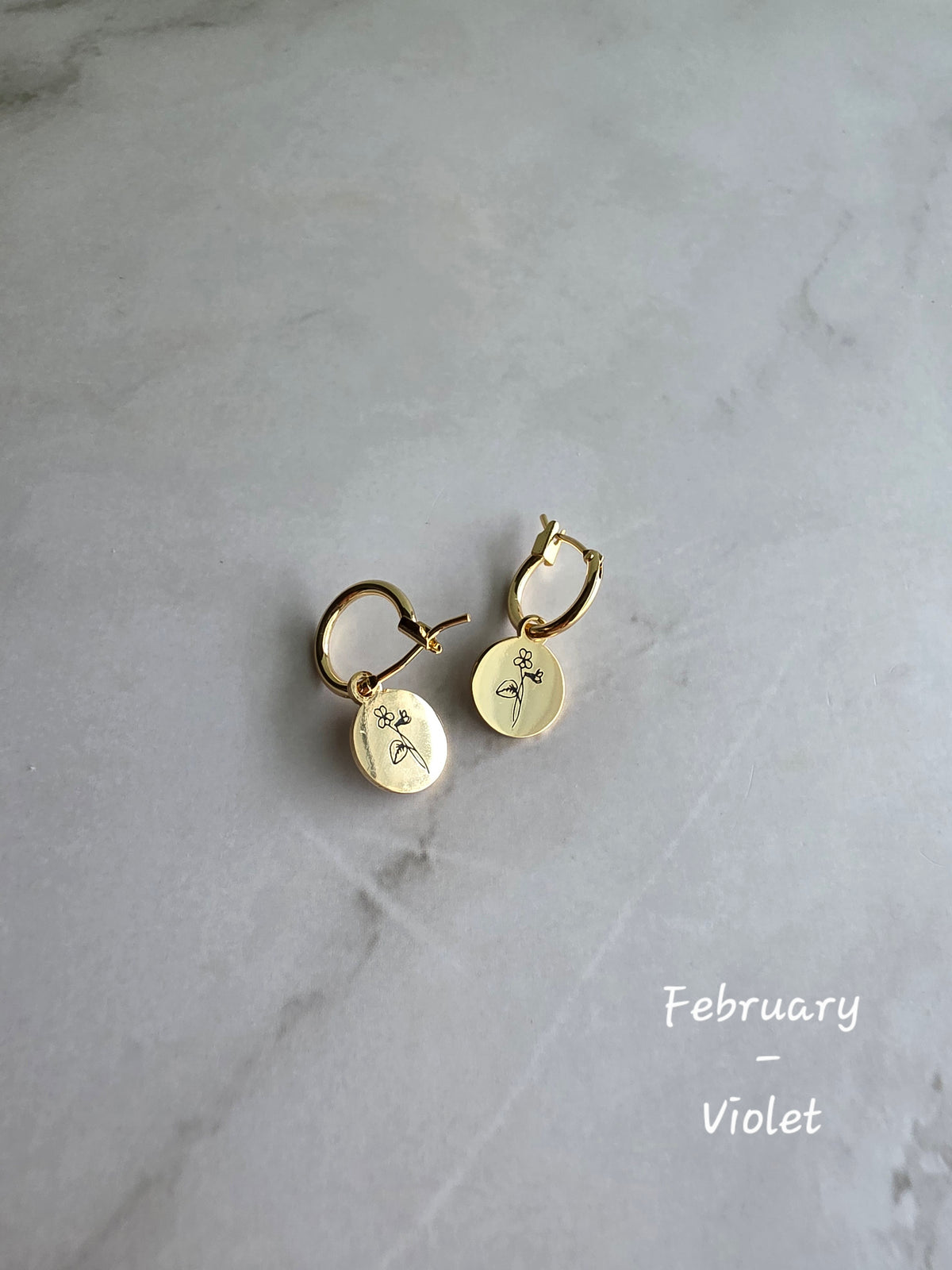 Minimalist birth flower earrings on 18K gold-plated huggie hoops.