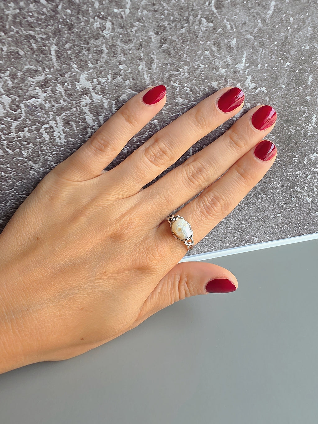 Hand with red nail polish wearing a silver ring on a textured surface