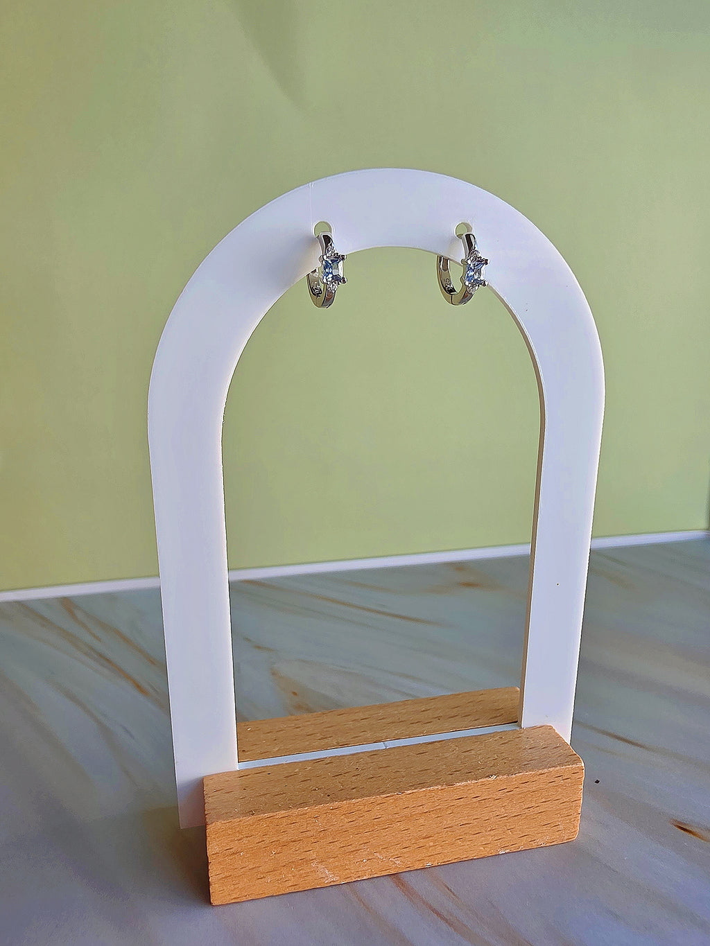 Earring display stand with wooden base and white arch, on a light green background.