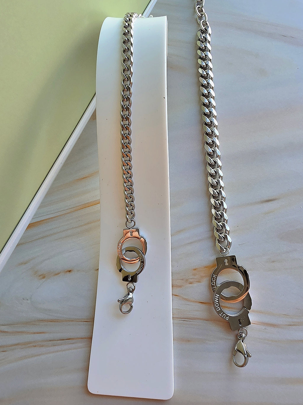 Two silver chain necklaces on a white stand with a light wooden background