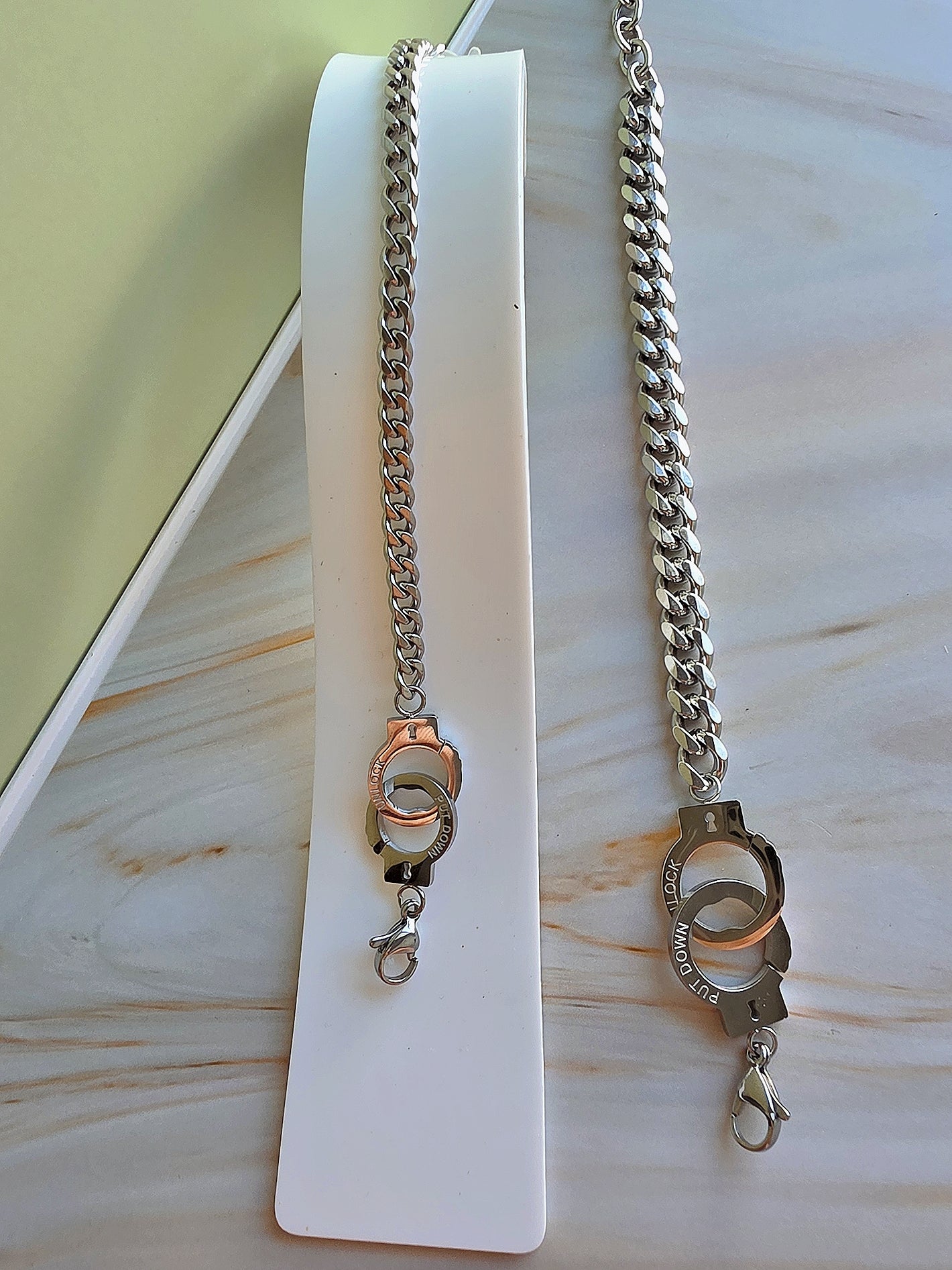 Two silver chain necklaces on a white stand with a light wooden background
