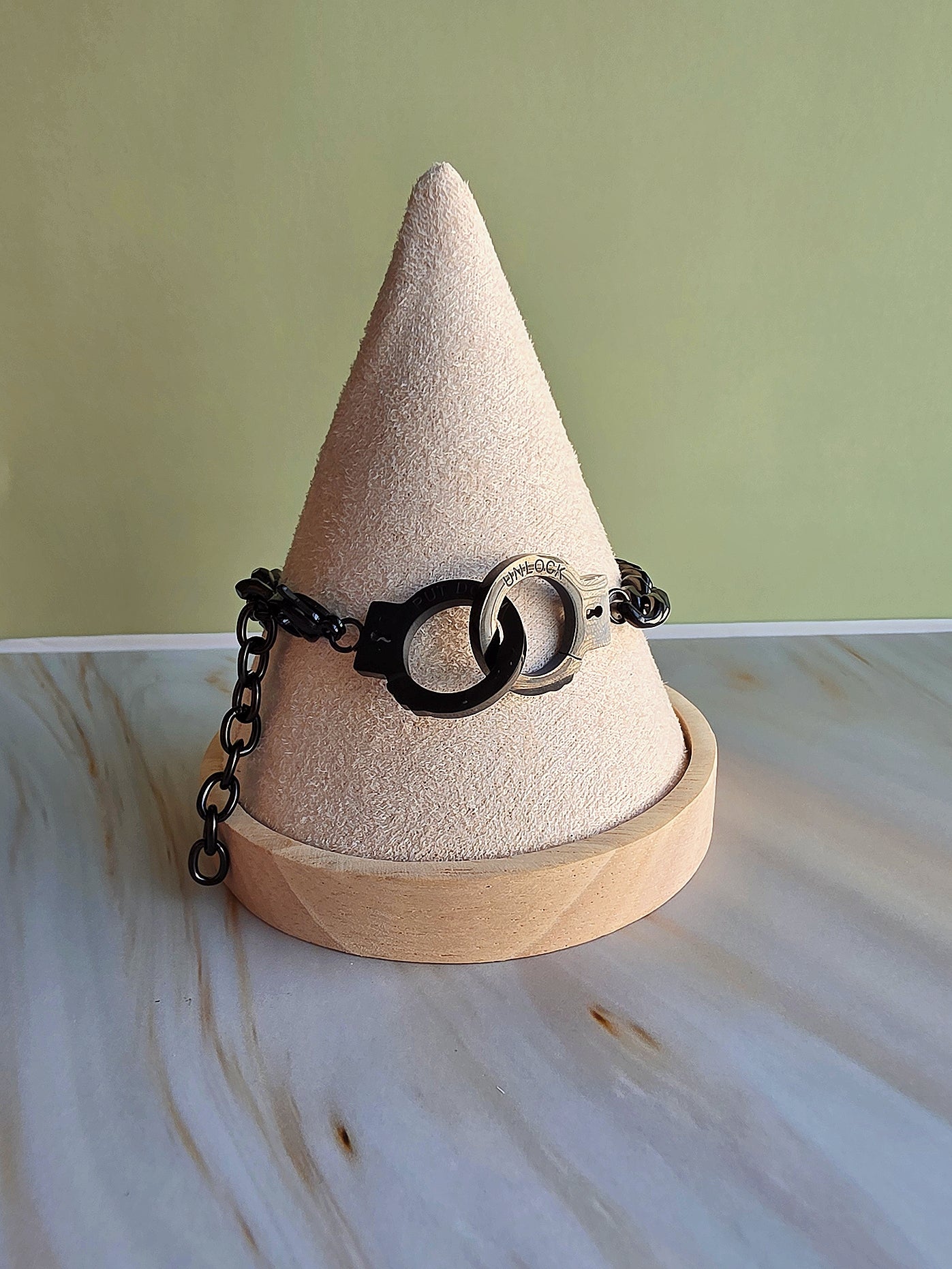 Beige cone-shaped jewelry holder with a black chain and circular object on a light-colored surface.
