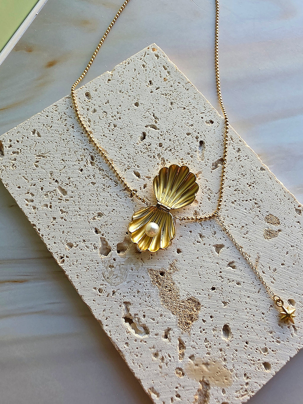 Elegant shell pendant necklace with a pearl charm and polished gold finish.