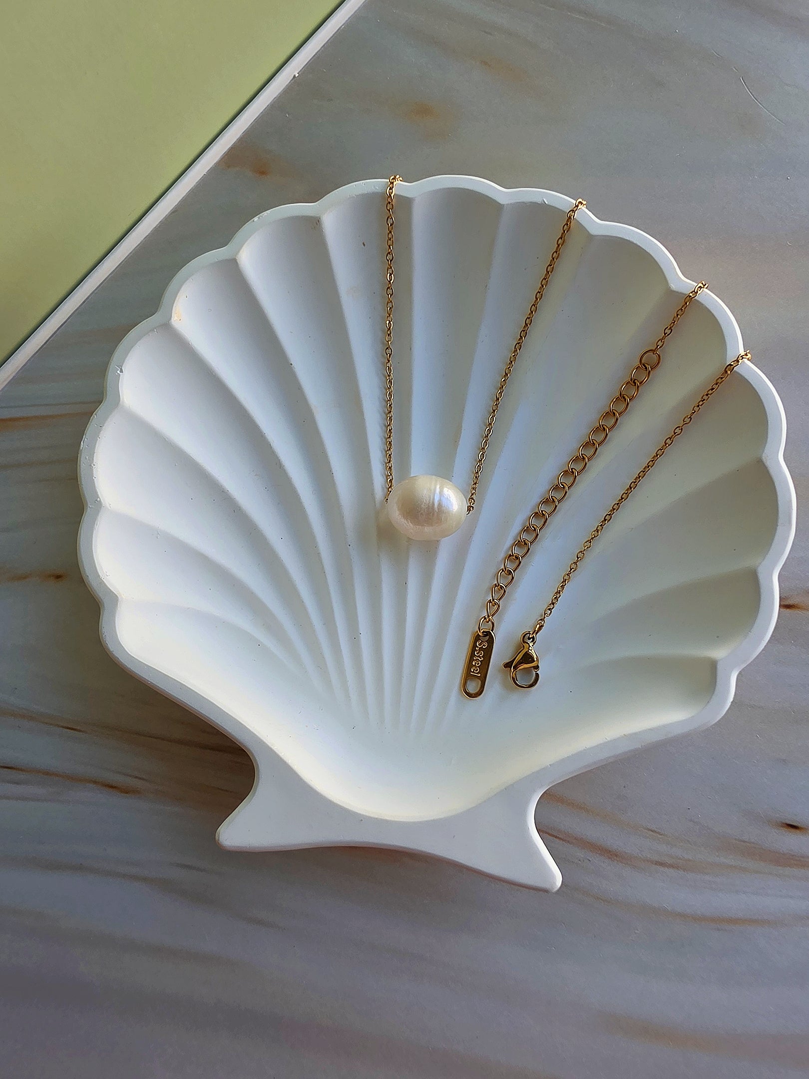 Gold necklace with a pearl pendant on a white shell-shaped stand.