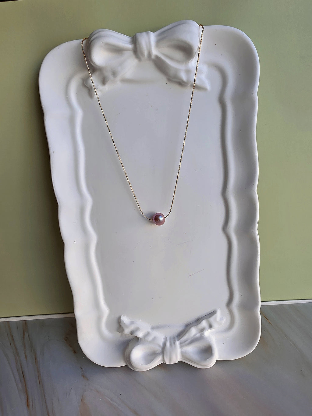 Necklace with a pink pendant on a decorative white plate against a green background