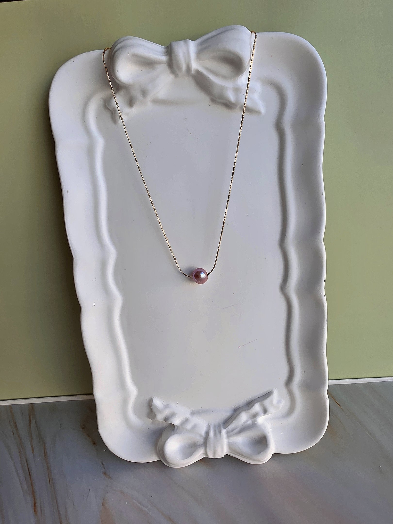 Necklace with a pink pendant on a decorative white plate against a green background