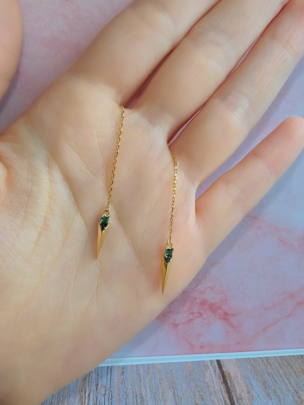 Minimalist spike threader earrings with emerald green gemstones and gold plating.