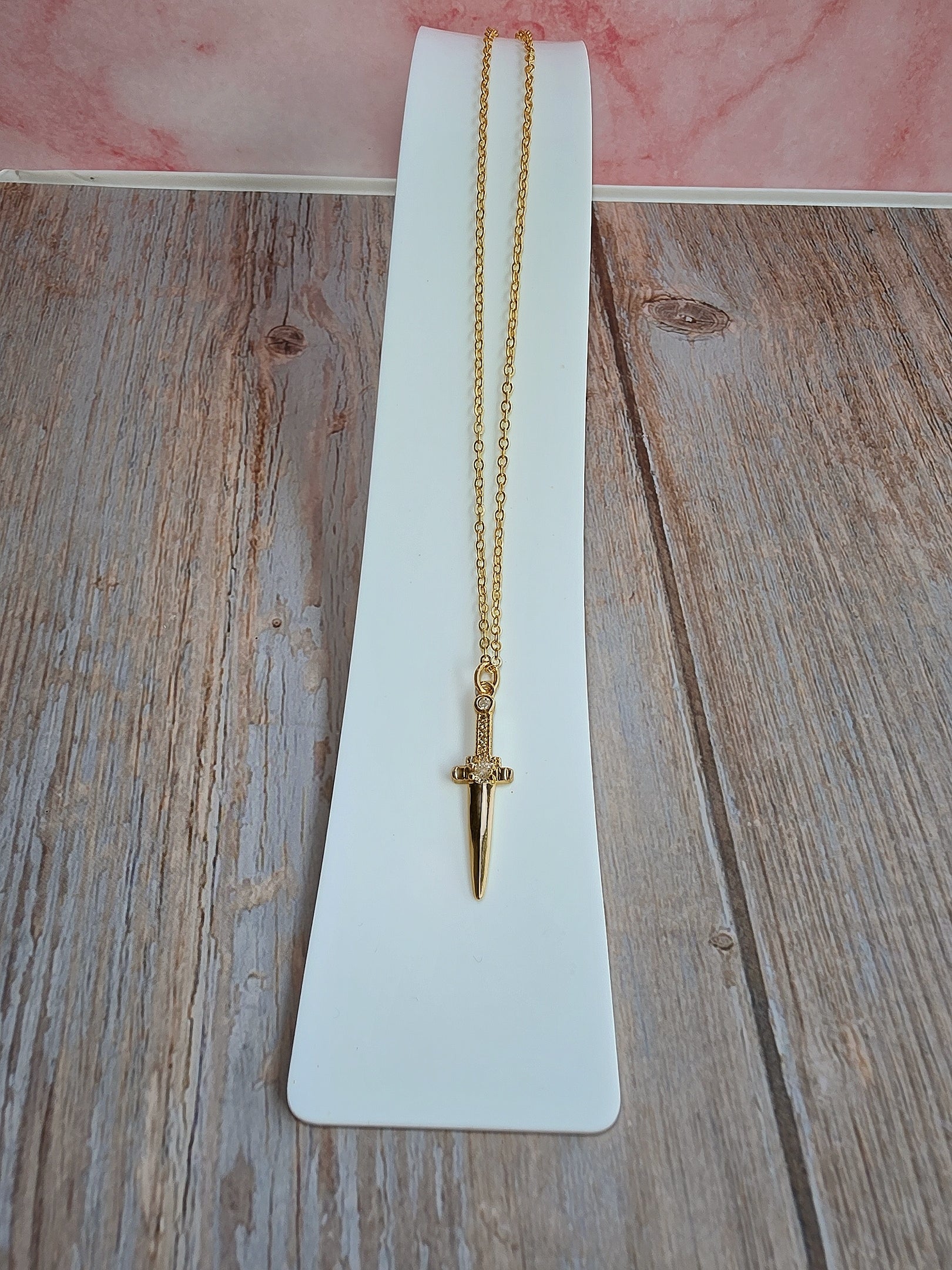 Elegant sword pendant necklace with cubic zirconia details and gold finish.