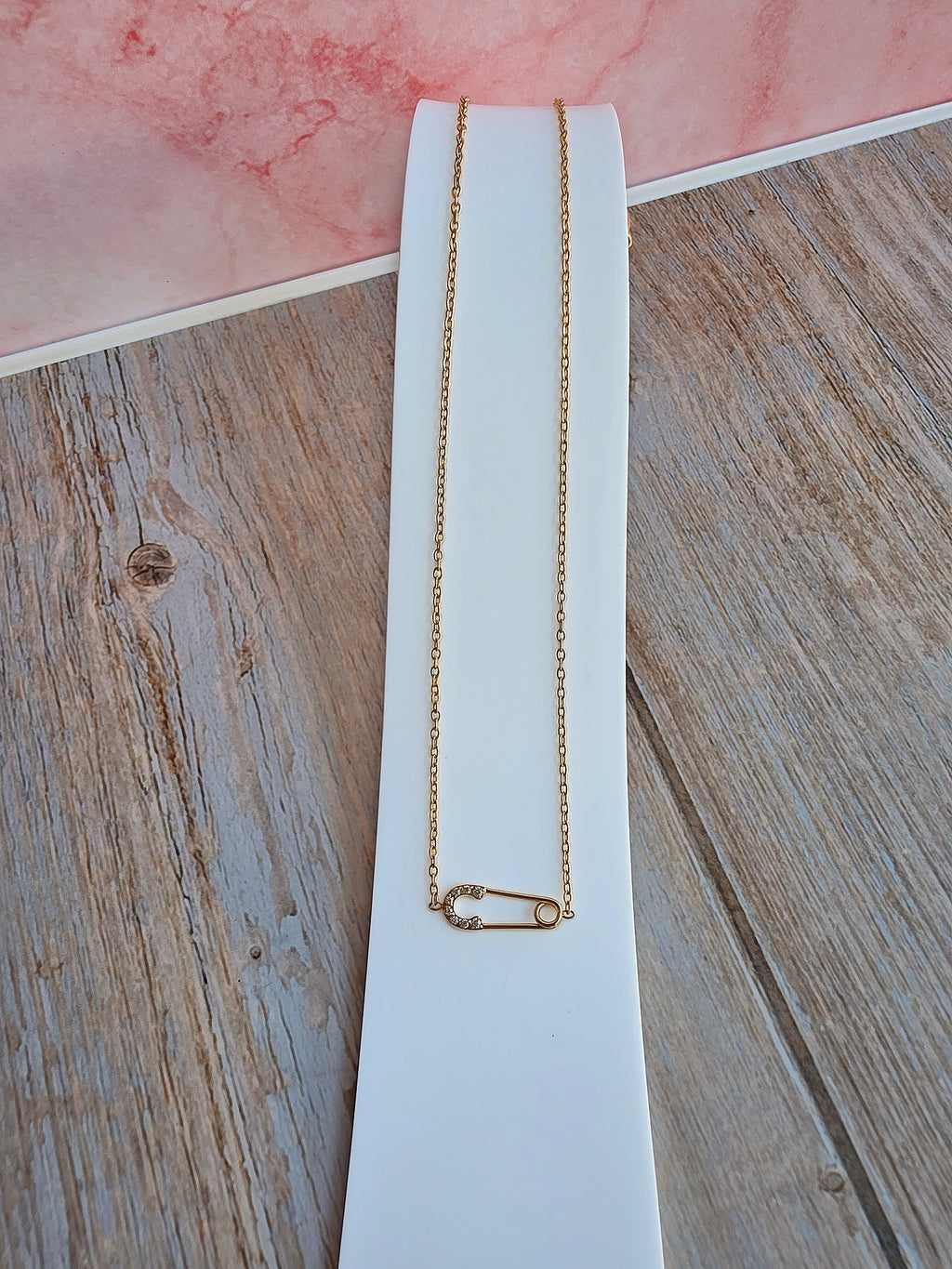 Elegant safety pin charm necklace with a delicate gold chain.