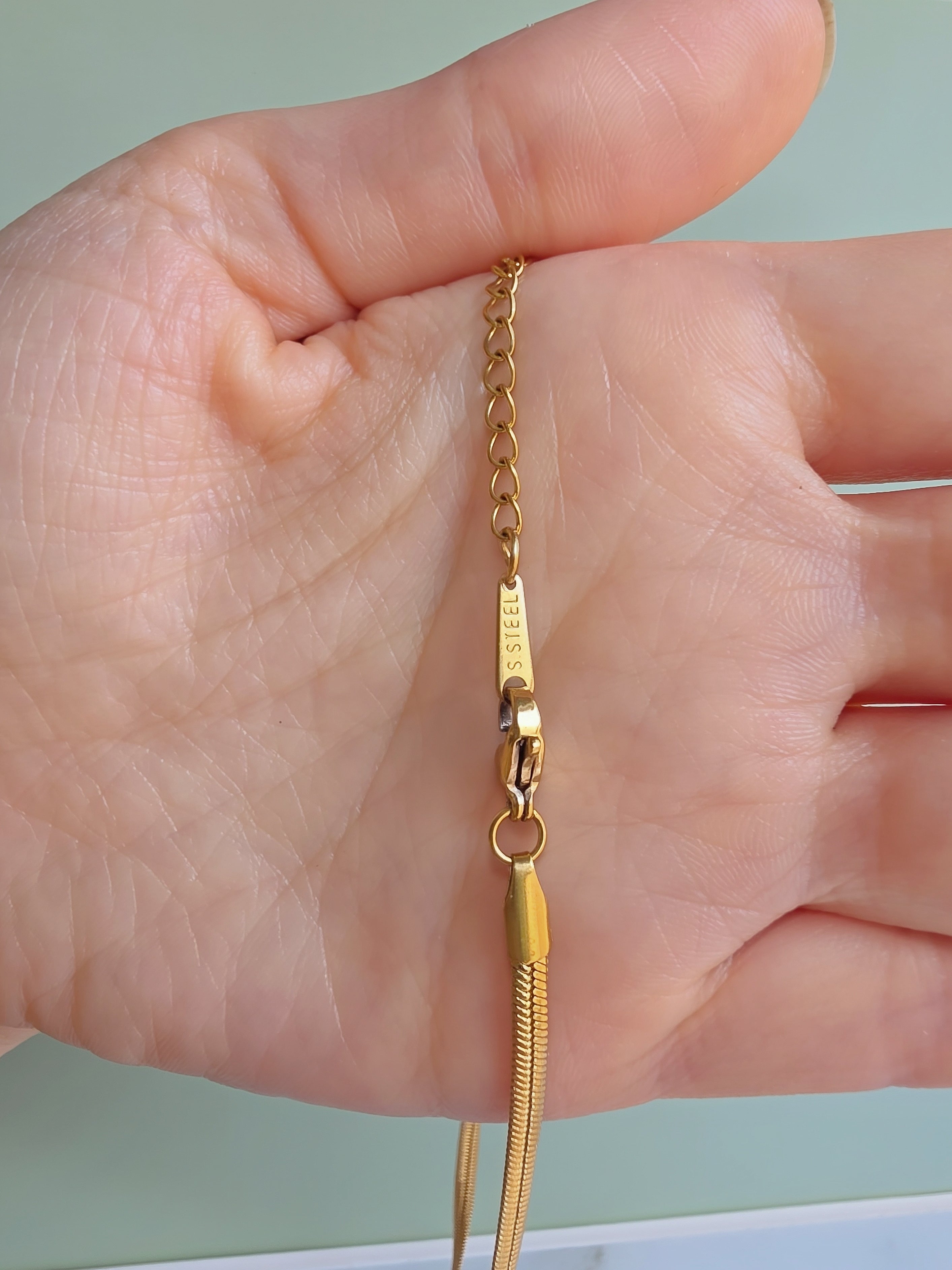A close-up of a hand holding a gold chain necklace with a lobster clasp and a textured snake-style pendant.
