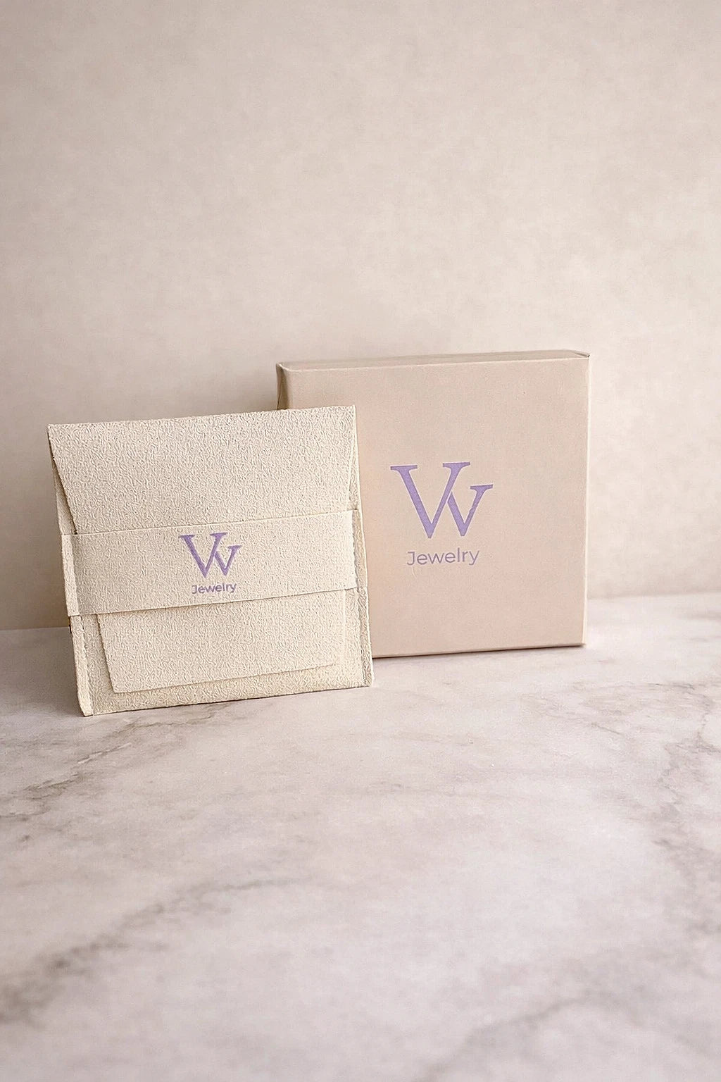 Two beige jewelry boxes with a logo on a marble surface