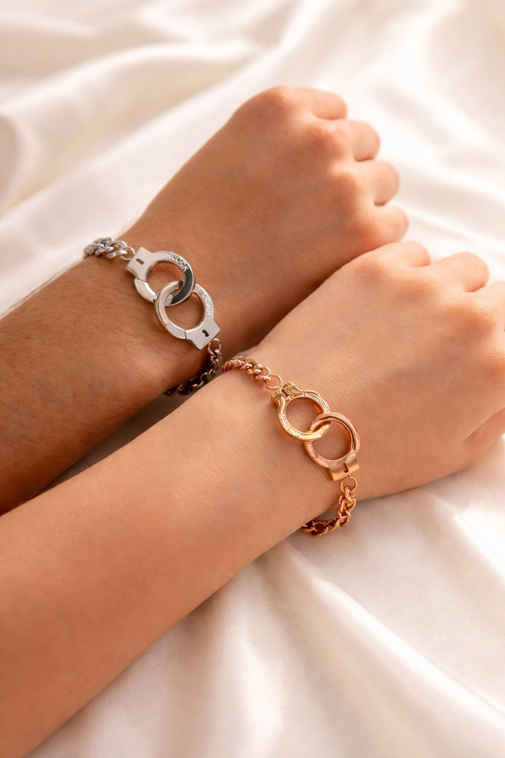 Two wrists wearing bracelets on a light fabric background