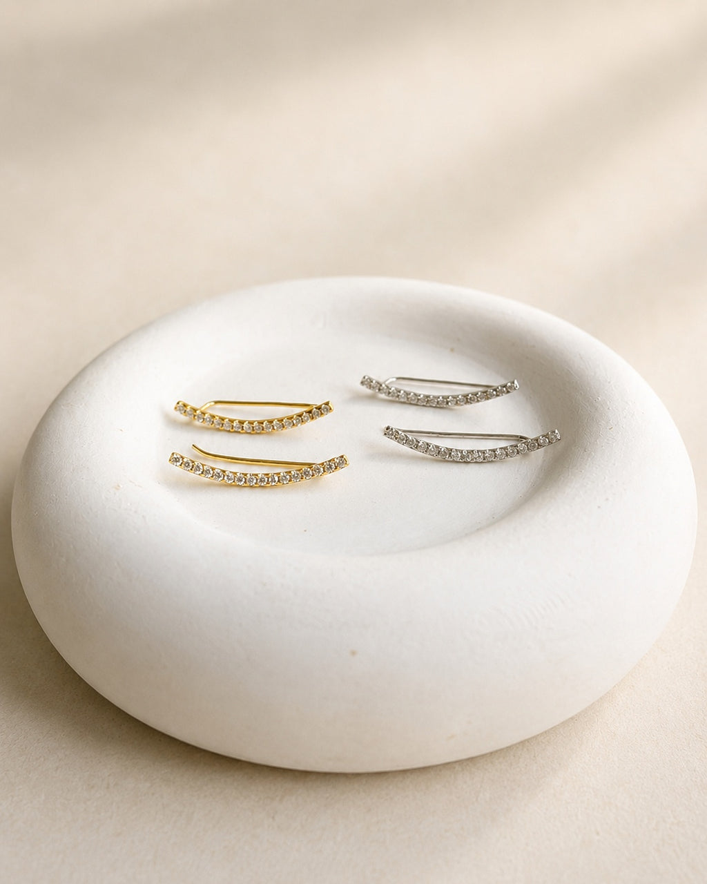 Curved CZ ear climber earrings displayed on a jewelry dish.